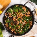 Large pan filled with risotto next to a loaf of bread, kale and a cutting board