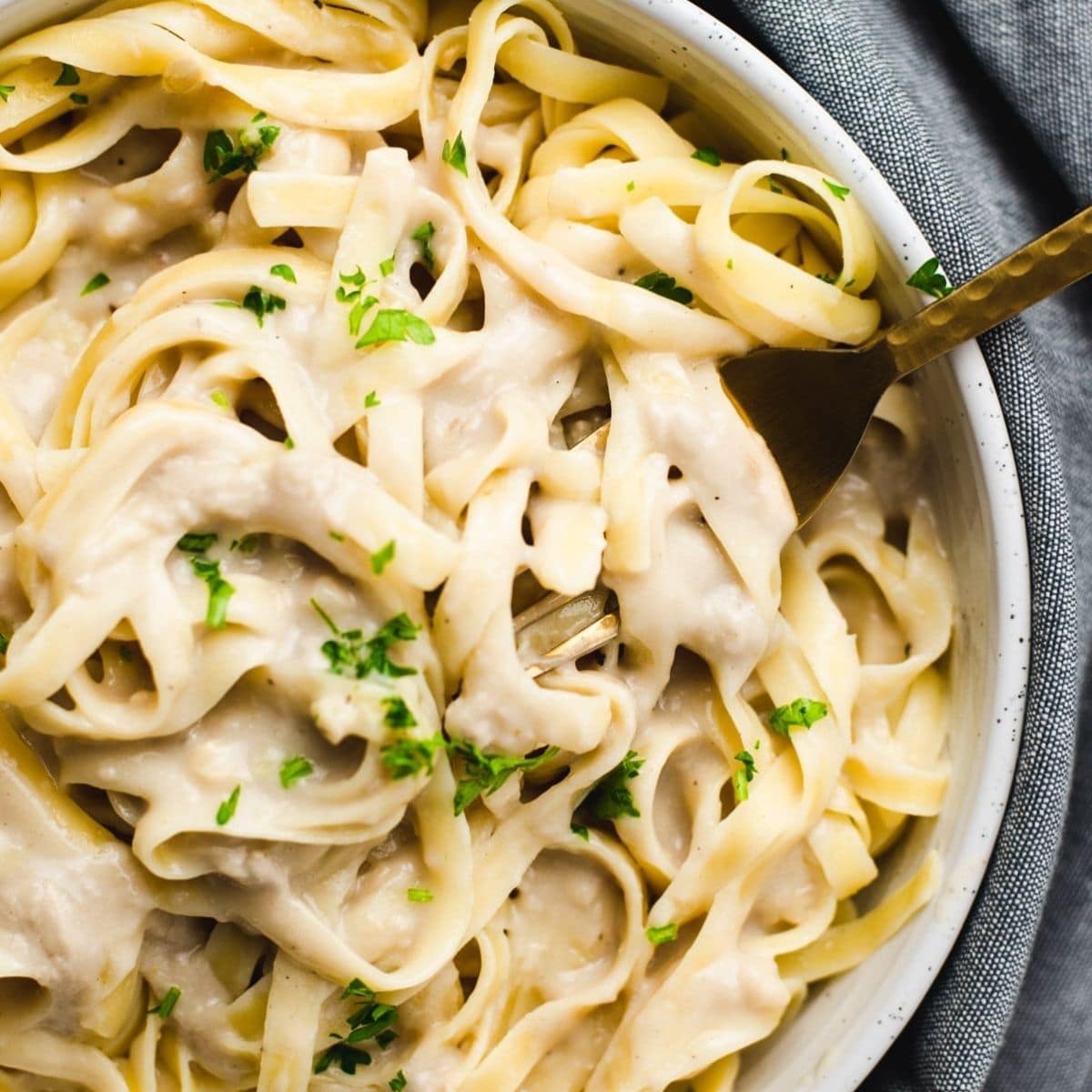 Large white bowl filled with fettucine topped in vegan alfredo and parsley.
