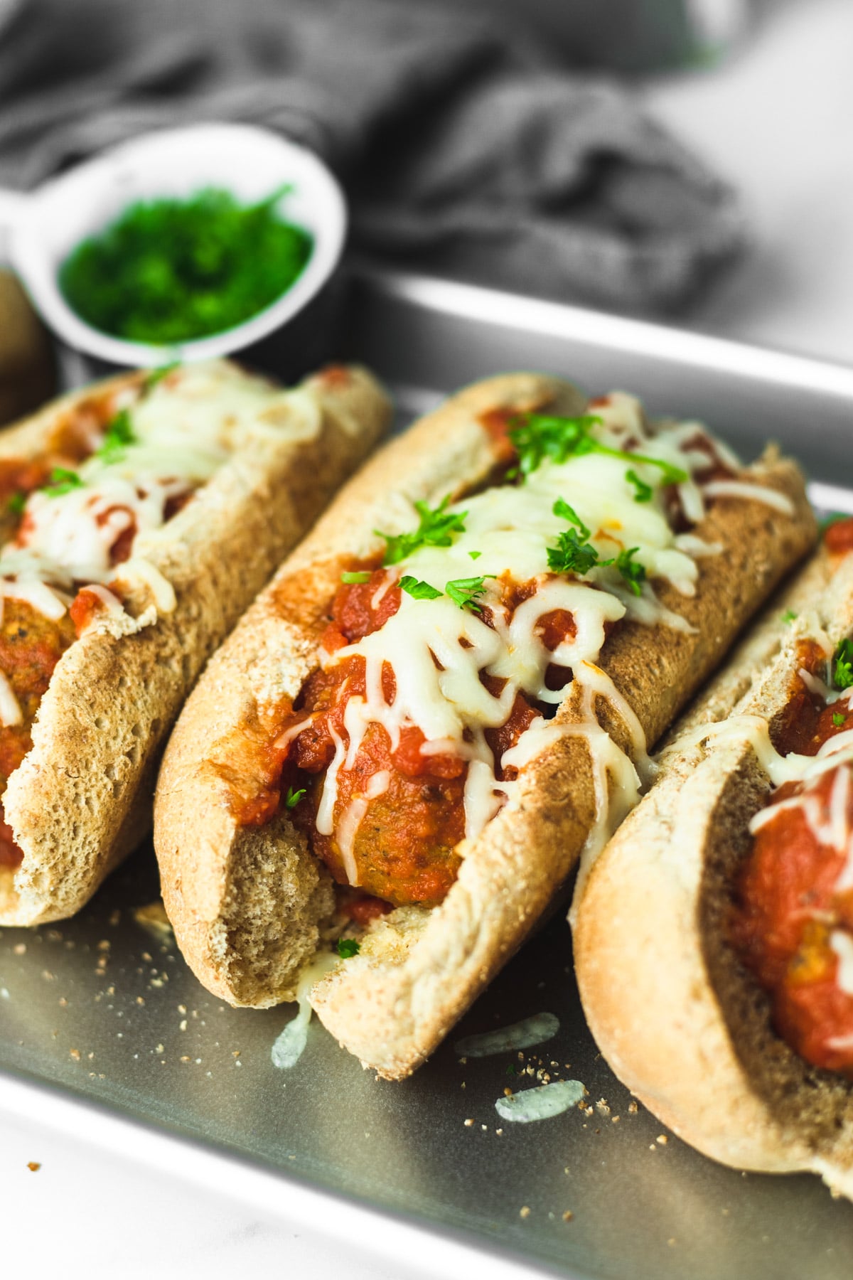 Three vegetarian meatball subs lined up on a silver sheet pan.