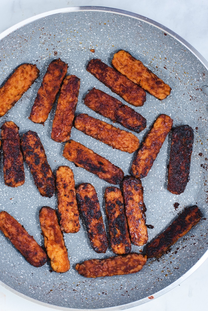 Cooked slices of tempeh in a gray skillet
