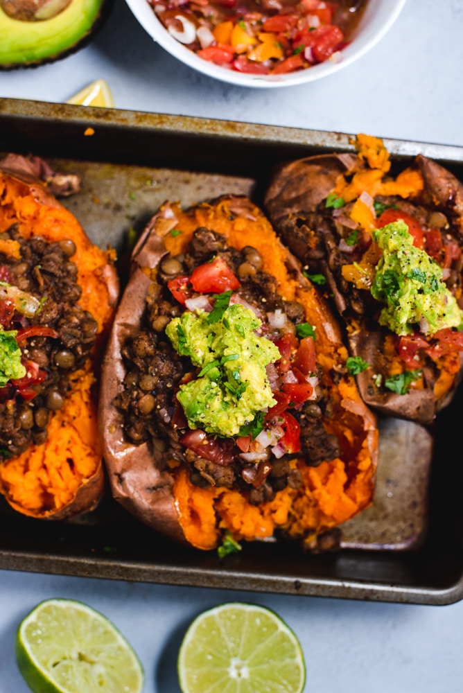 Stuffed sweet potato in a metal pan next to limes and an avocado