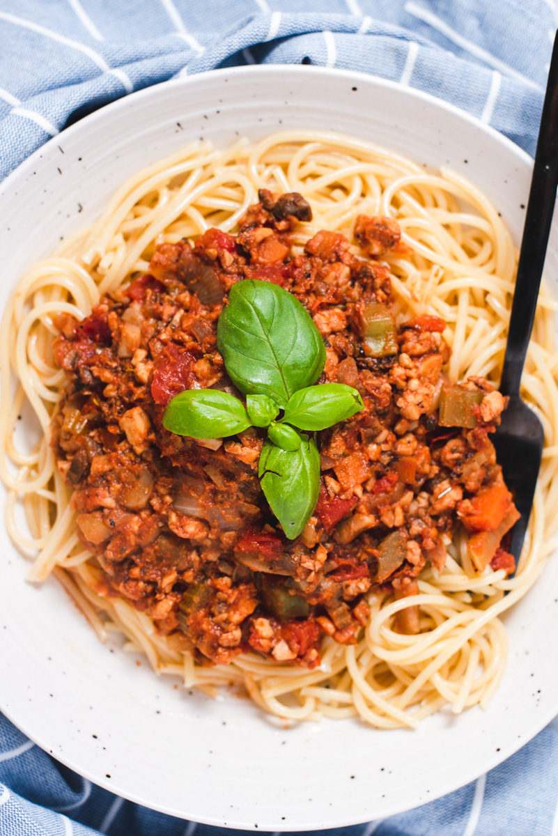 Large serving of spaghetti topped with bolognese sauce and fresh basil