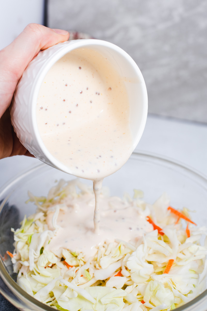 White bowl with mayonnaise being poured onto shredded cabbage.