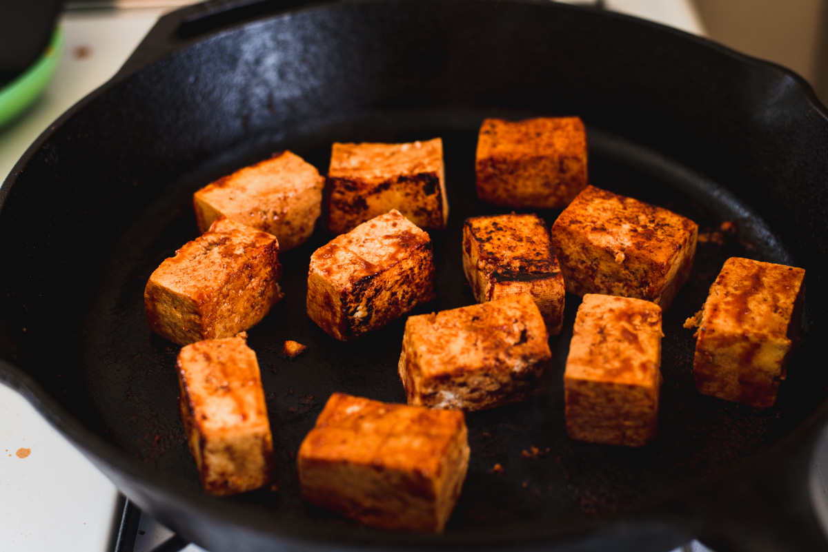 Cubes of tofu sauteeing a large cast iron skillet.