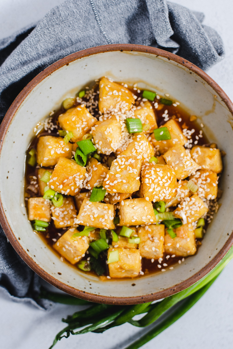 Large grey bowl filled with baked tofu and green onions.