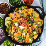 Cast iron skillet filled with nachos surrounded by bowls of nacho ingredients
