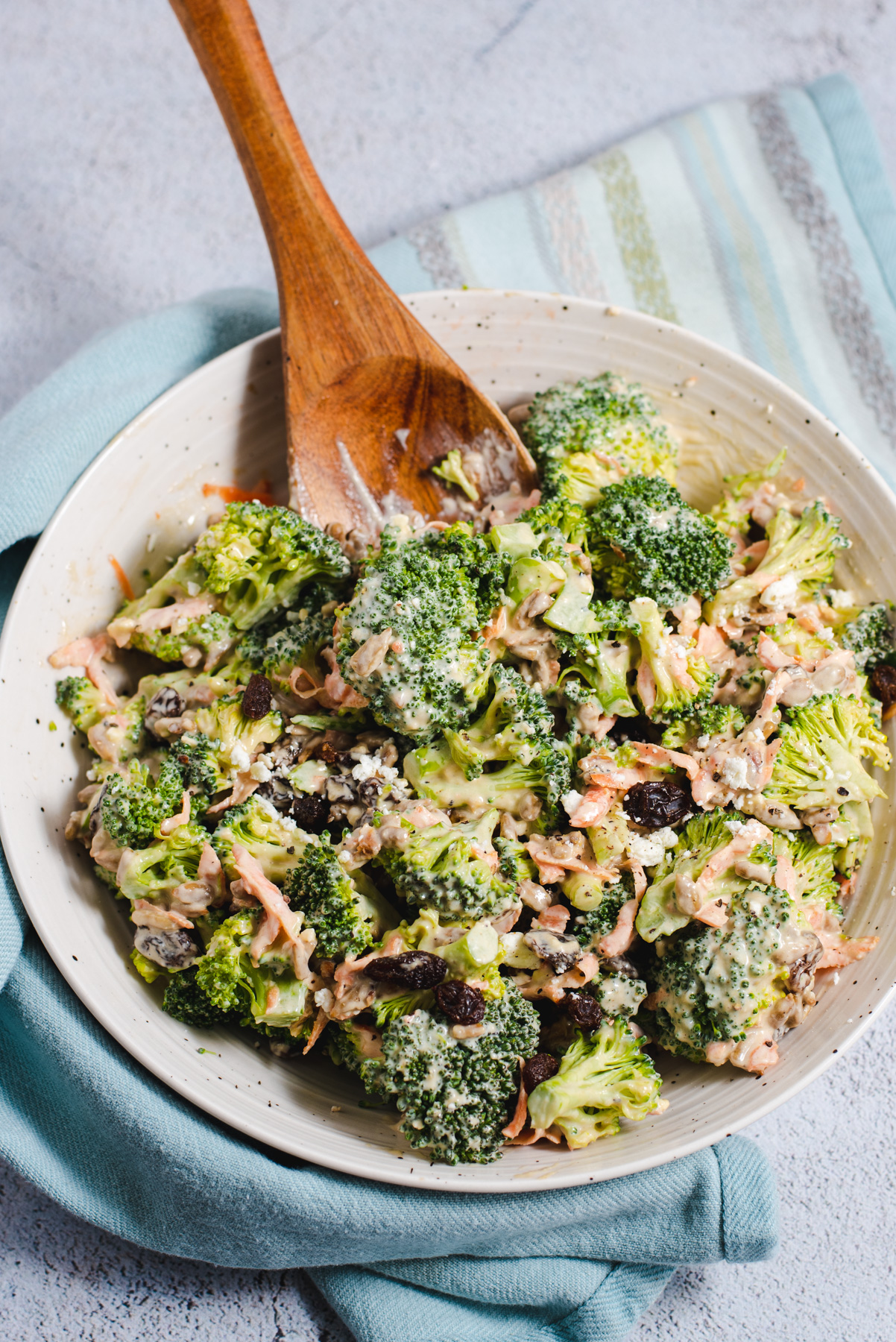 Broccoli salad in a white bowl with a wooden serving spoon.
