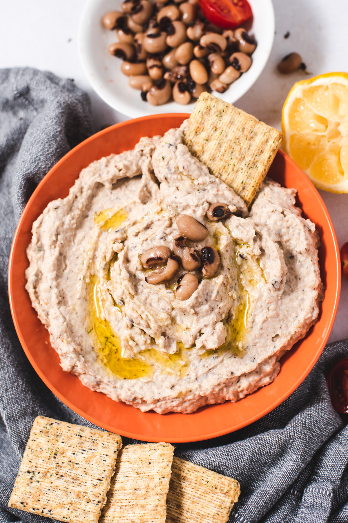 Black eyed pea hummus in a peach-colored bowl surrounded by crackers.