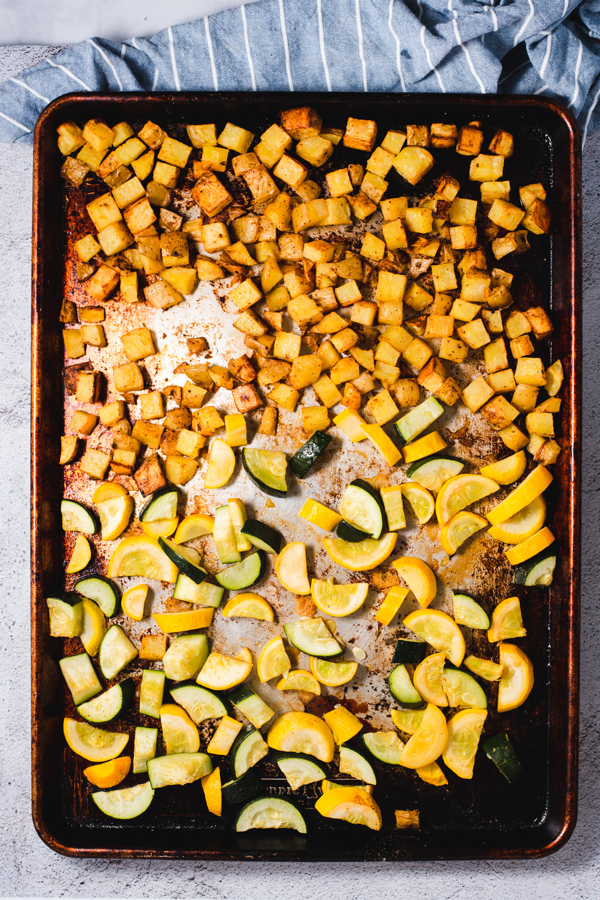 Sliced squash, zucchini, and potatoes on a metal sheet pan.