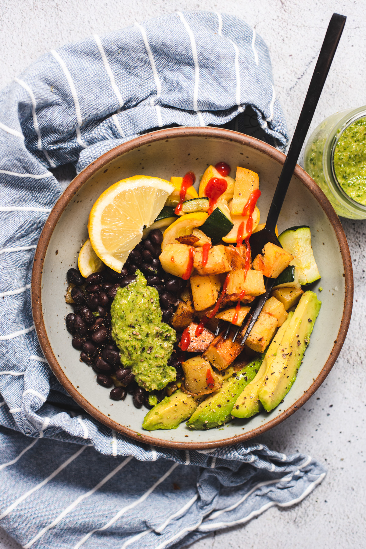 Bowl filled with pesto, avocado, roasted potatoes, black beans and roasted squash.
