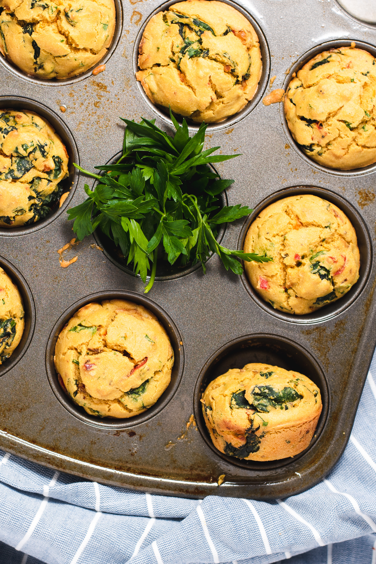 Muffins and fresh parsley in a metal muffin tin.