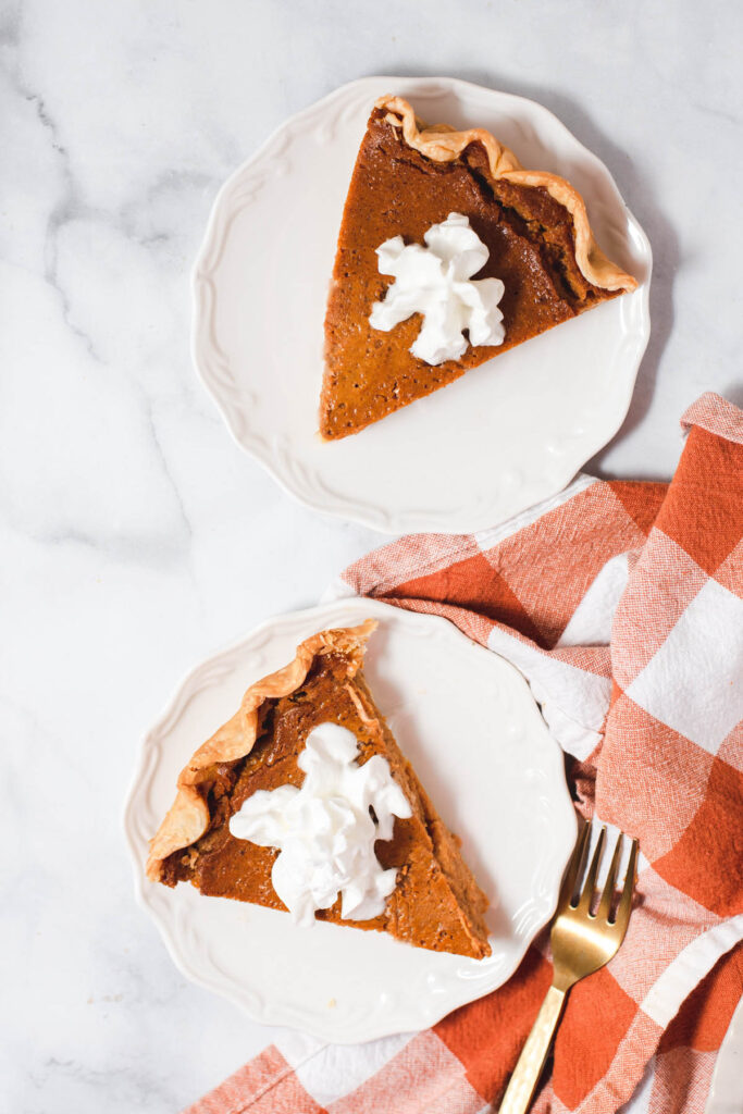 Overhead view of two slices of pumpkin pie on white plates