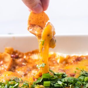 Frito scooping chili cream cheese dip from a white baking dish.
