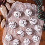 Overhead view of twelve chocolate crackles on a piece of crinkled wax paper surrounded by ornaments and green ribbon