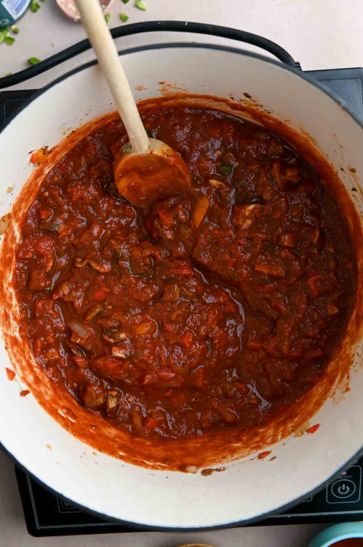 Deep red tomato sauce in a Dutch oven with a wooden spoon.