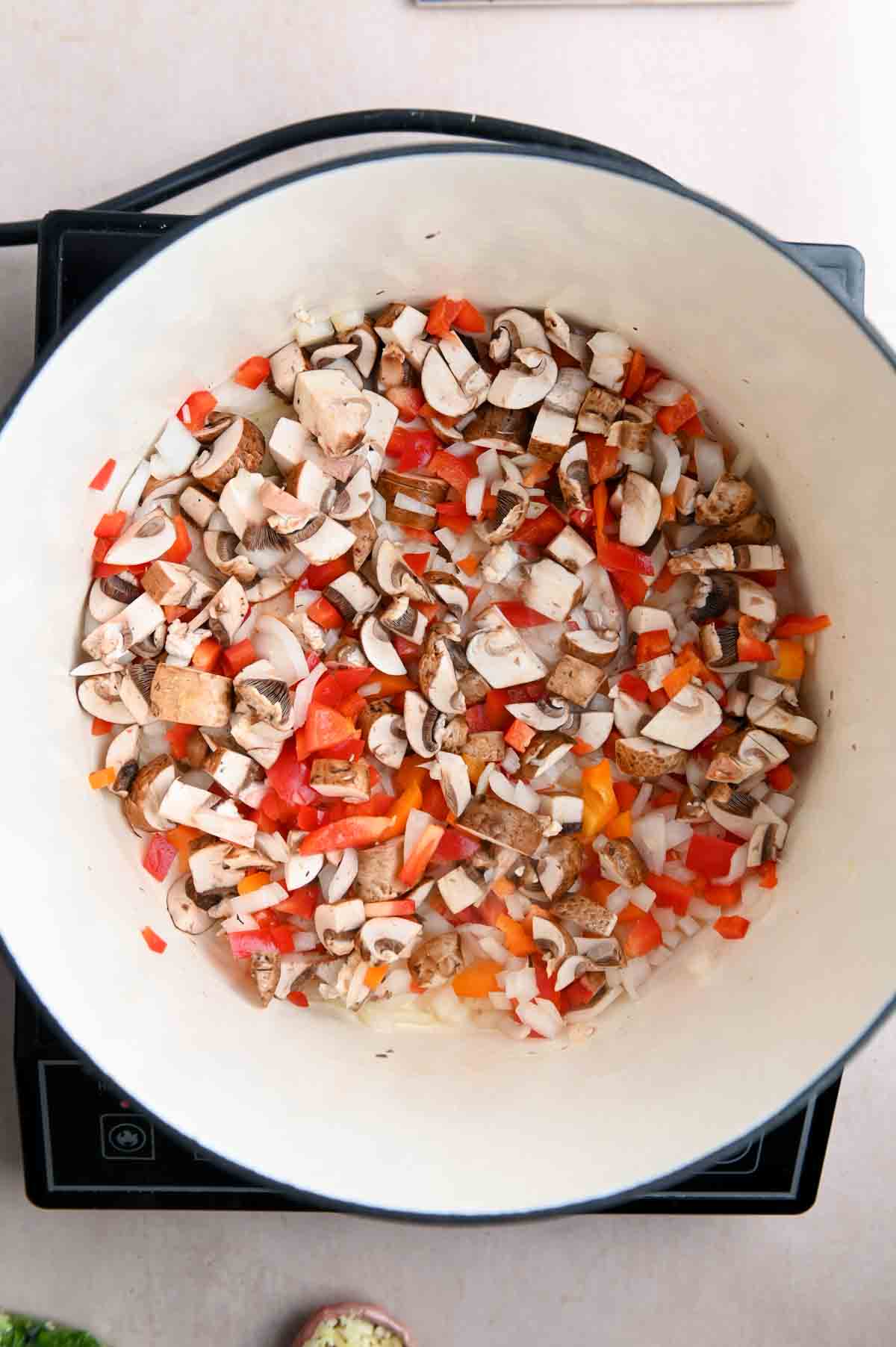 Diced mushrooms, peppers, and onions in a Dutch oven.