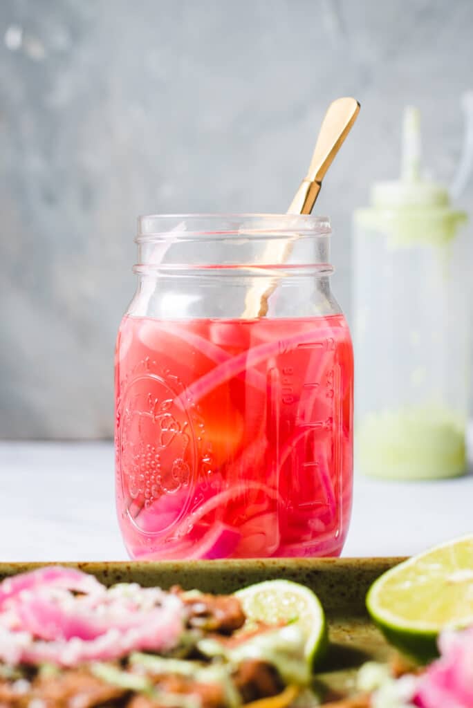 Glass jar filled with pickled red onions and gold fork