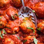 Close up of vegan meatballs in tomato sauce being lifted with a slotted spoon.
