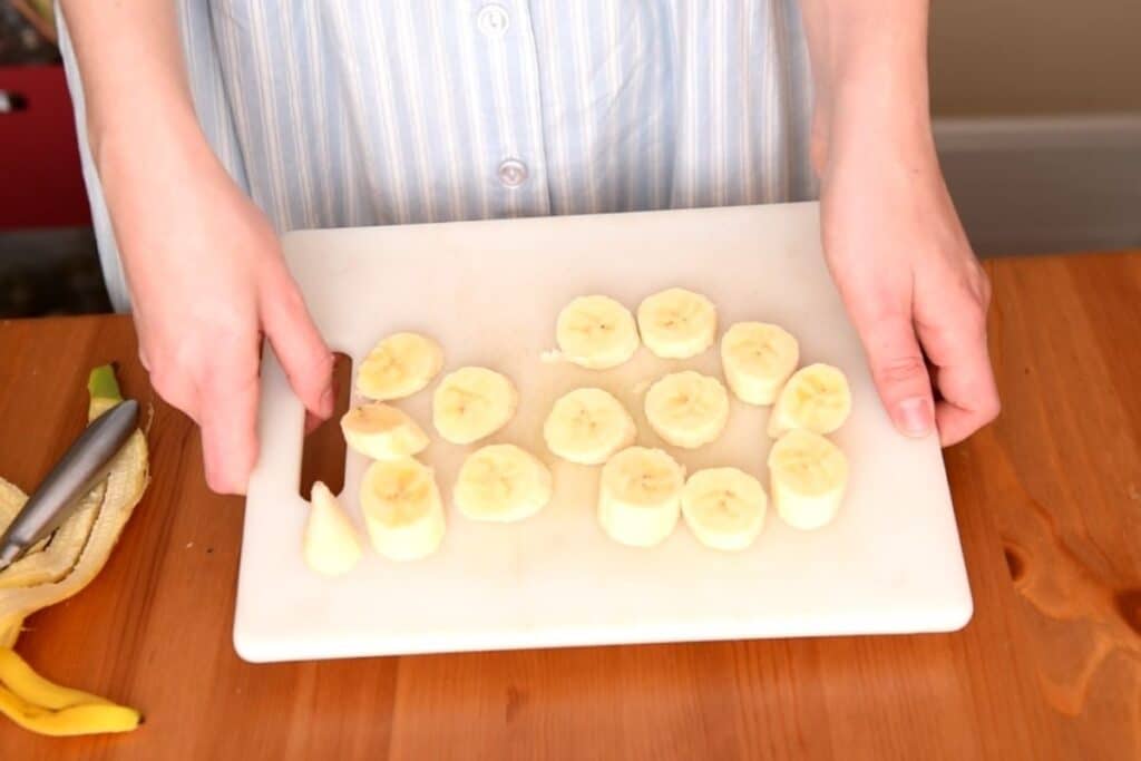 Cutting board with sliced bananas being held above a wood table