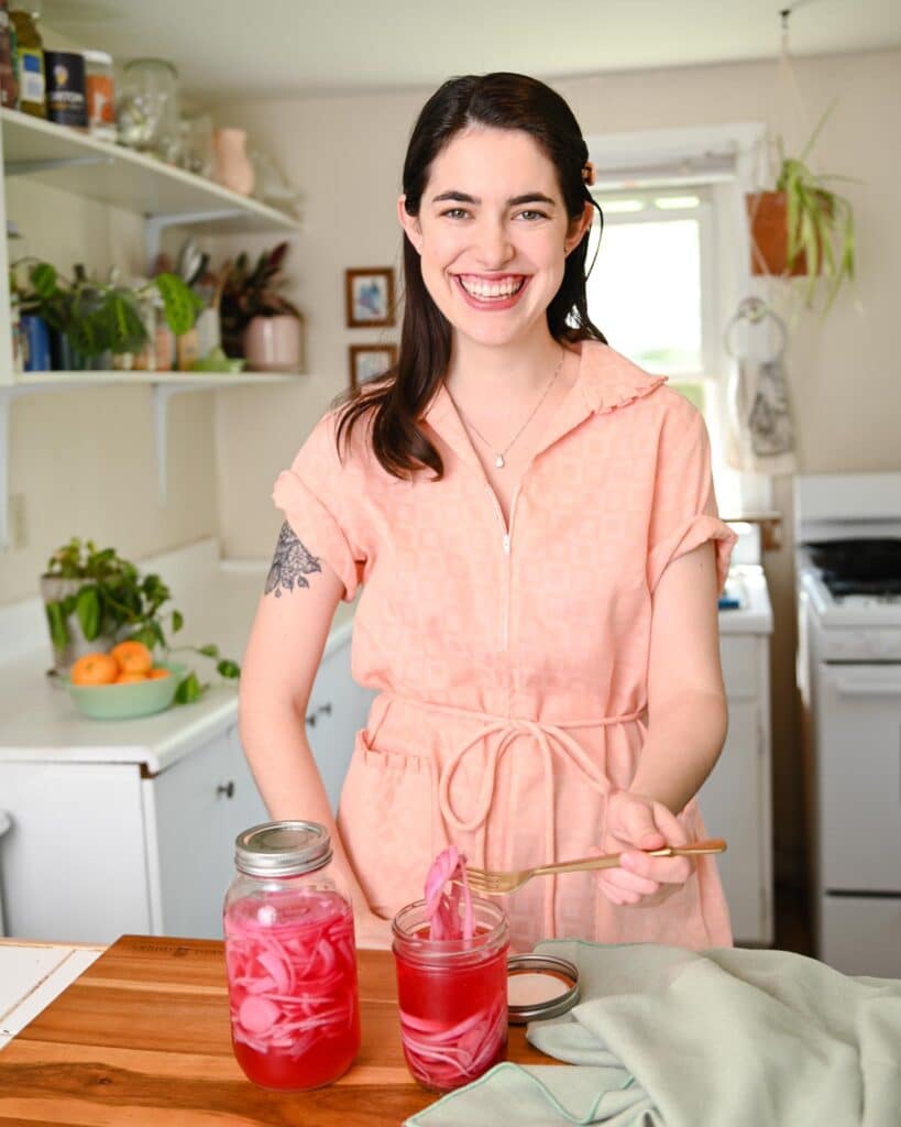 Smiling woman in pink dress in front of jar of pickled red onions