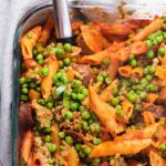 Overhead view of penne pasta with peas in a glass baking dish