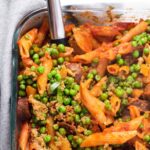 Overhead view of penne pasta with peas in a glass baking dish