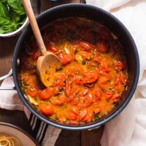 Cherry tomato sauce with wooden spoon in a black sauce pot