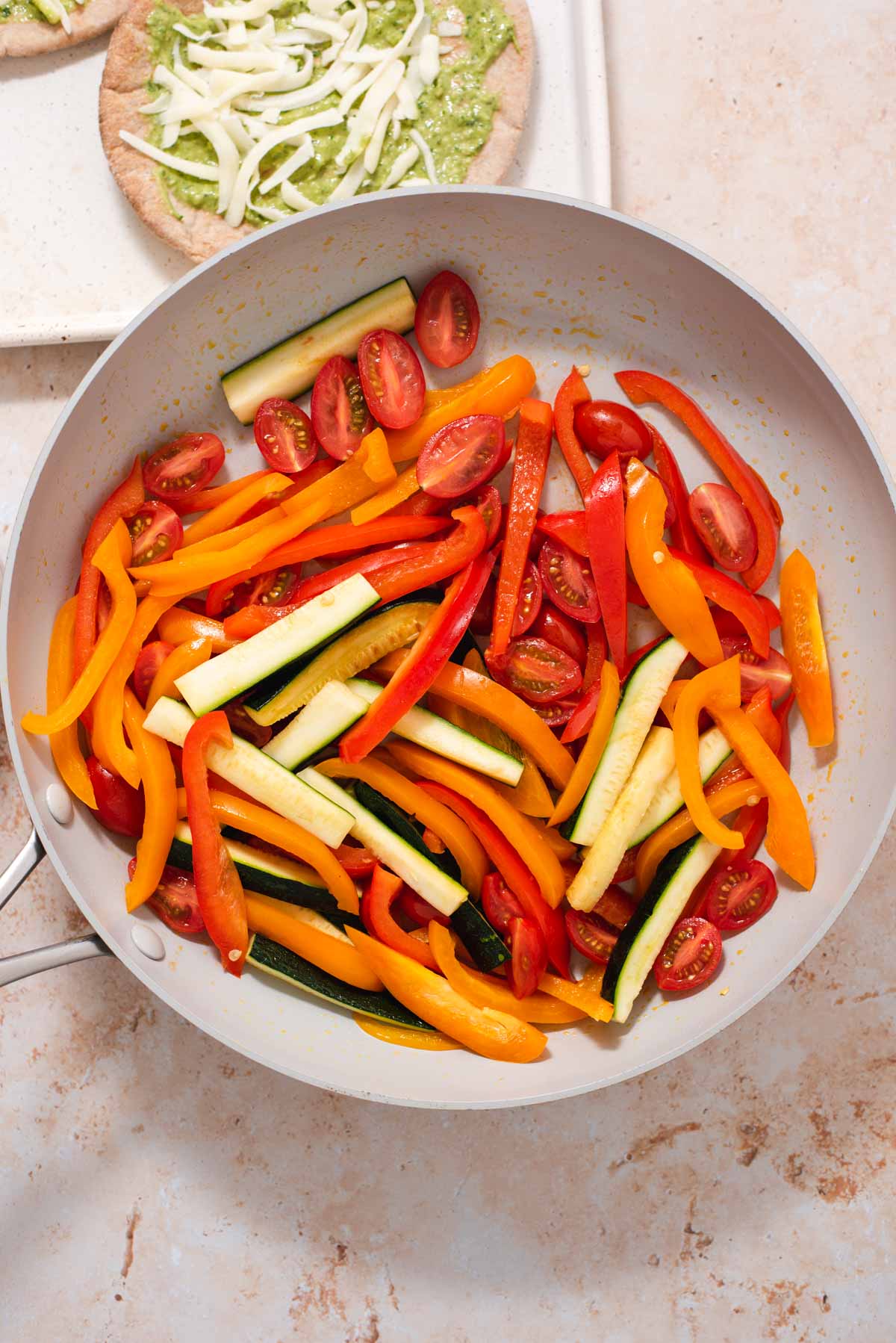 Overhead view of red and orange bell pepper and zucchini in a saute pan
