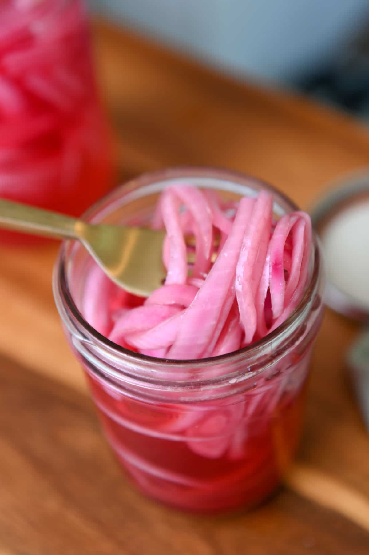 Gold fork lifting slices of pickled red onion out of a glass jar.