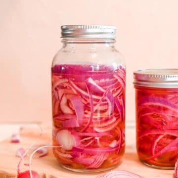 Quart sized jar of pickled onions in pink juice in front of a pink background