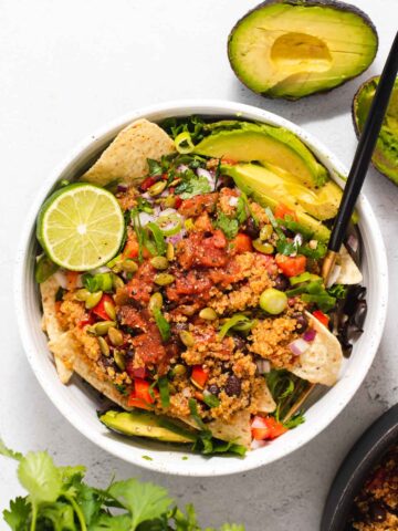 Overhead view of large white bowl filled with quinoa salad, avocado and a life half