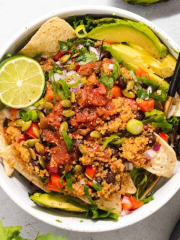 Overhead view of large white bowl filled with quinoa salad, avocado and a life half