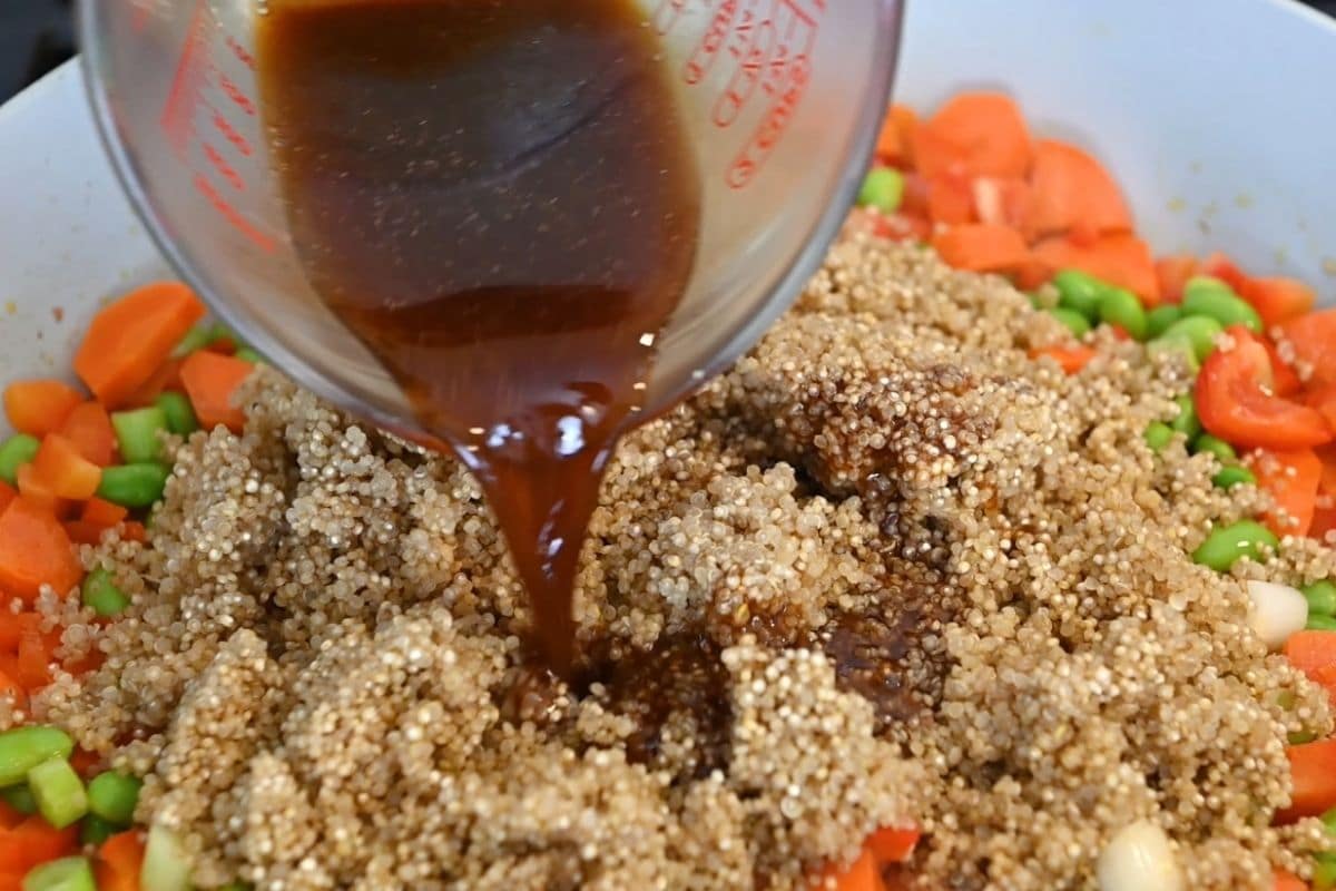 Teriyaki sauce being poured onto vegetables in a skillet