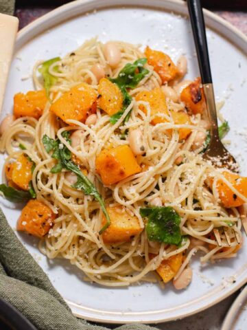 Overhead view of white plate with pile of angel hair pasta and butternut squash.