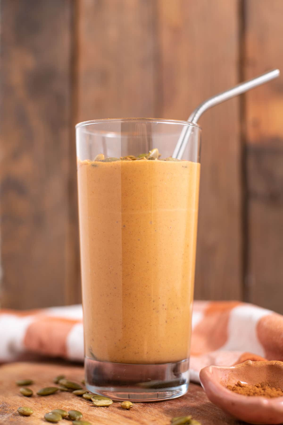 Side view of tall glass filled with orange smoothie in front of a wooden background