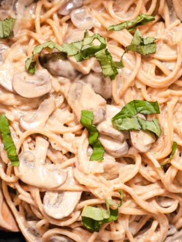 Close up of fettucine coated in a creamy white sauce with basil on top