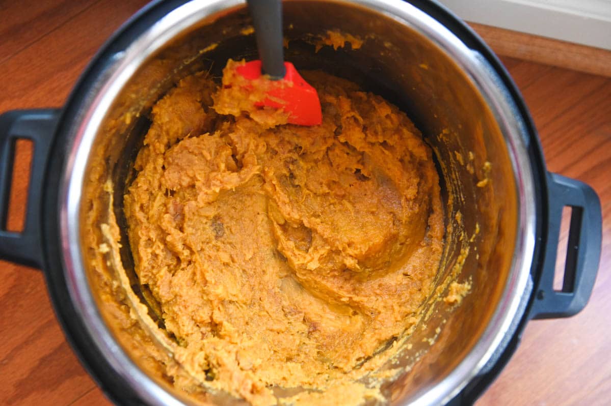 Mashed sweet potatoes in Instant Pot with red spatula.