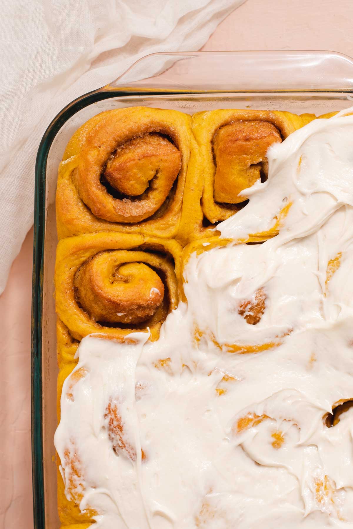 Glass pan of frosted pumpkin cinnamon rolls with two unfrosted cinnamon rolls at the top