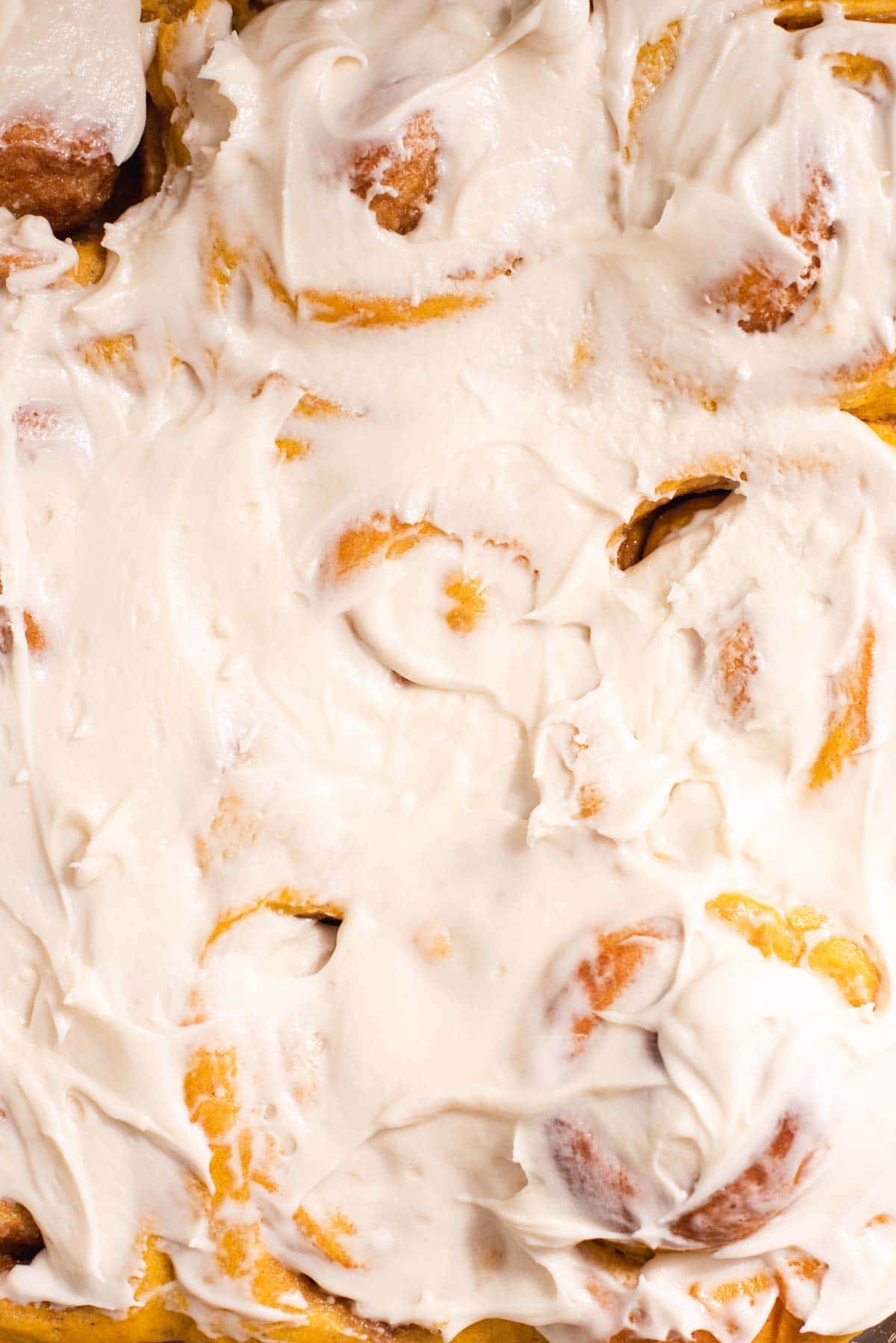 Close up of thick white frosting on light orange cinnamon rolls.