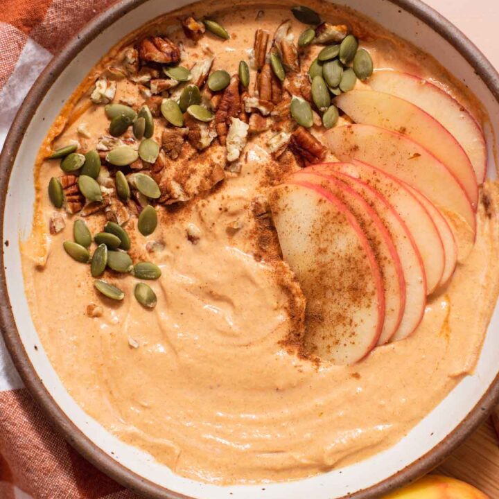 Overhead view of creamy orange dip in a white bowl with pumpkin seeds and apple slices