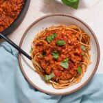 White bowl filled with spaghetti and red lentil sauce on a blue cloth