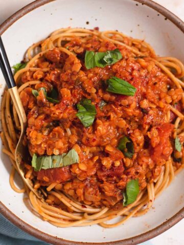 Spaghetti topped with red lentil tomato sauce and pieces of basil in a white bowl