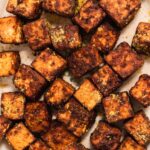 Close up of golden brown tofu cubes dusted with yellow nutritional yeast