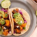 Two corn tortillas filled with butternut squash, black beans, guacamole and cilantro