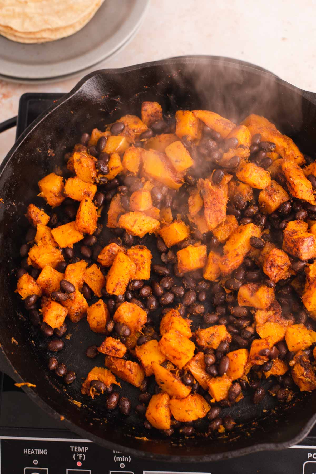 Diced butternut squash and black beans cooking in a black cast iron skillet