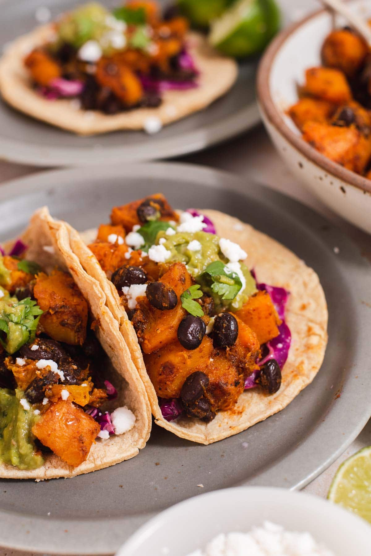 Two corn tortillas filled with butternut squash, black beans, and guacamole