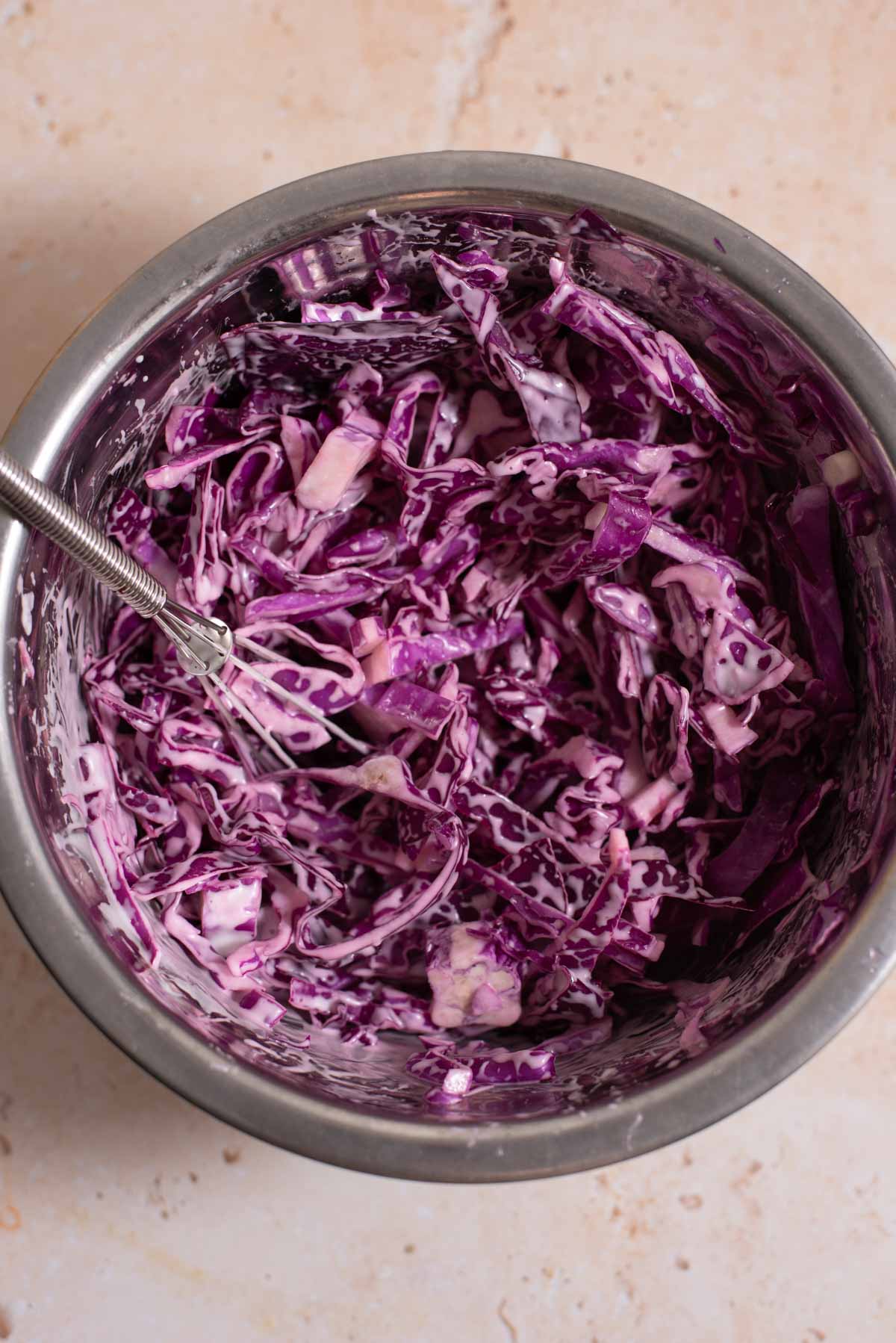 Shredded purple cabbage coleslaw with a small whisk in a metal mixing bowl