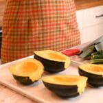 Four sliced acorn squash on a white sheet pan with a person in the background
