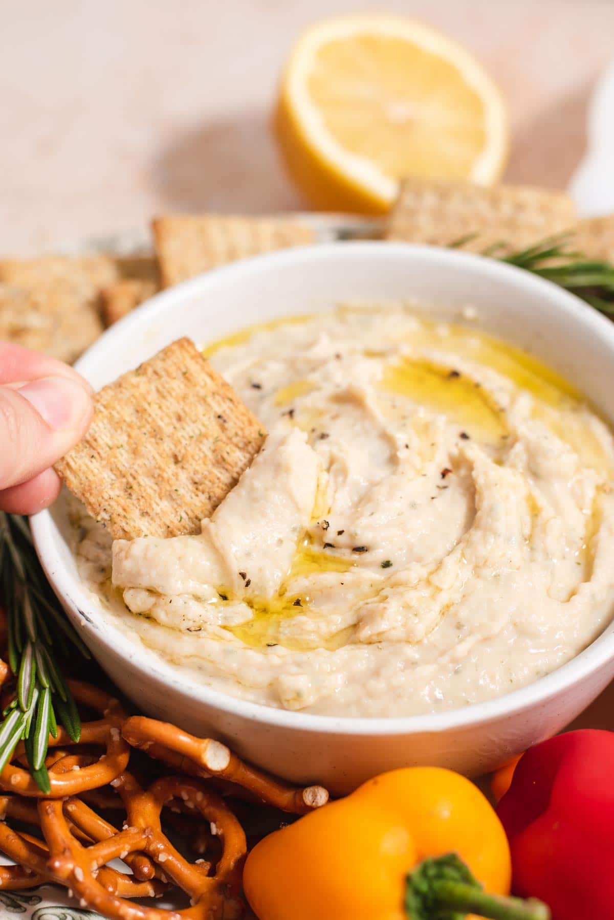Triscuit being dipped into a white bowl with white bean dip topped with olive oil