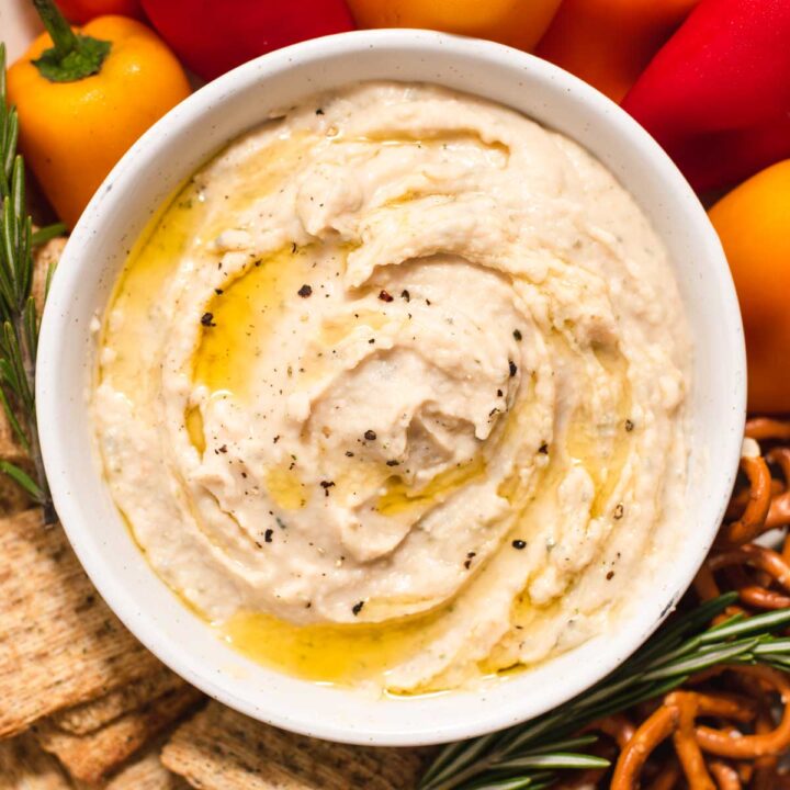 Overhead view of white bowl filled with white bean dip next to crackers and baby bell peppers